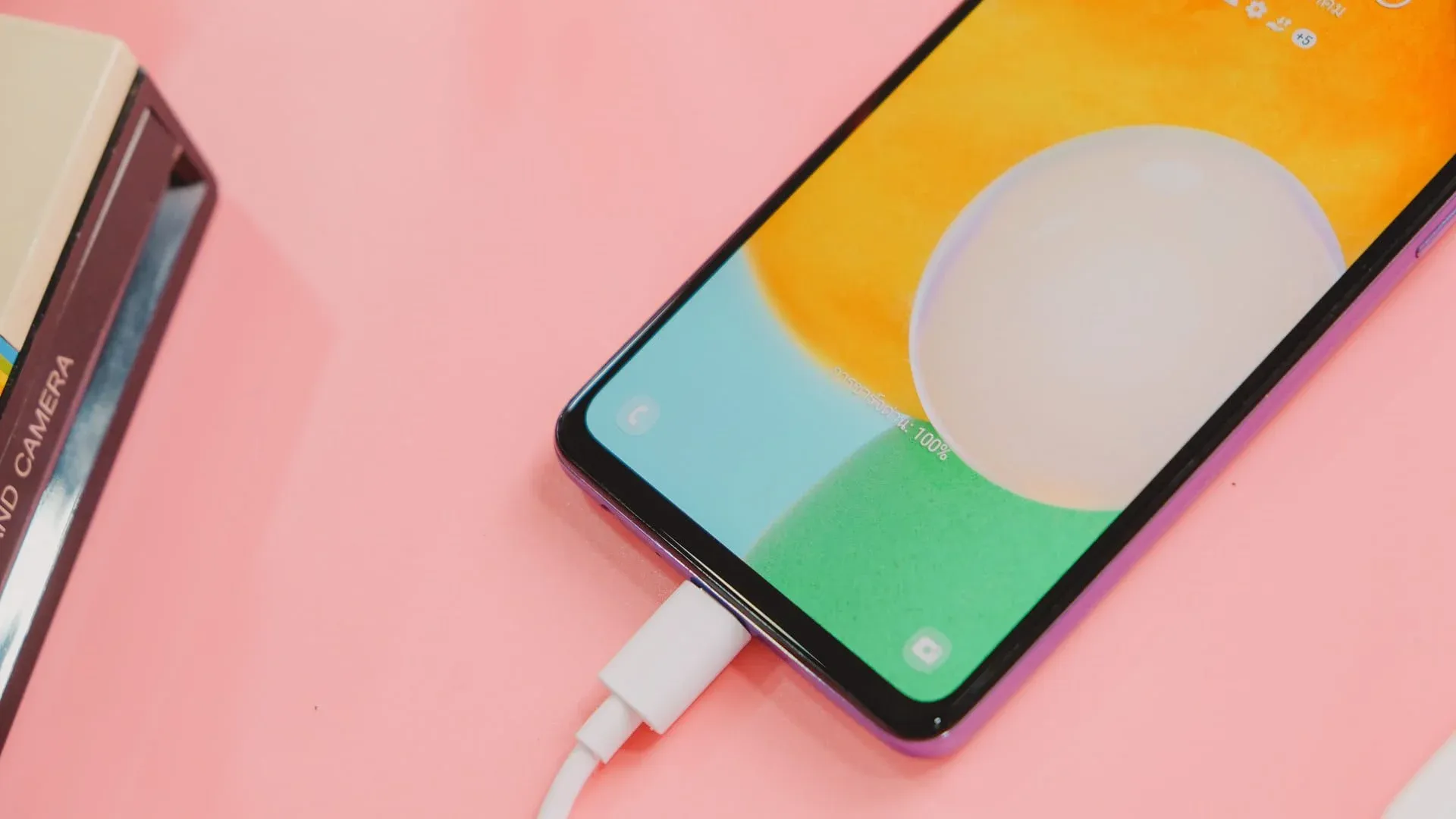 Celular Samsung Galaxy A52 conectado ao carregador em mesa rosa