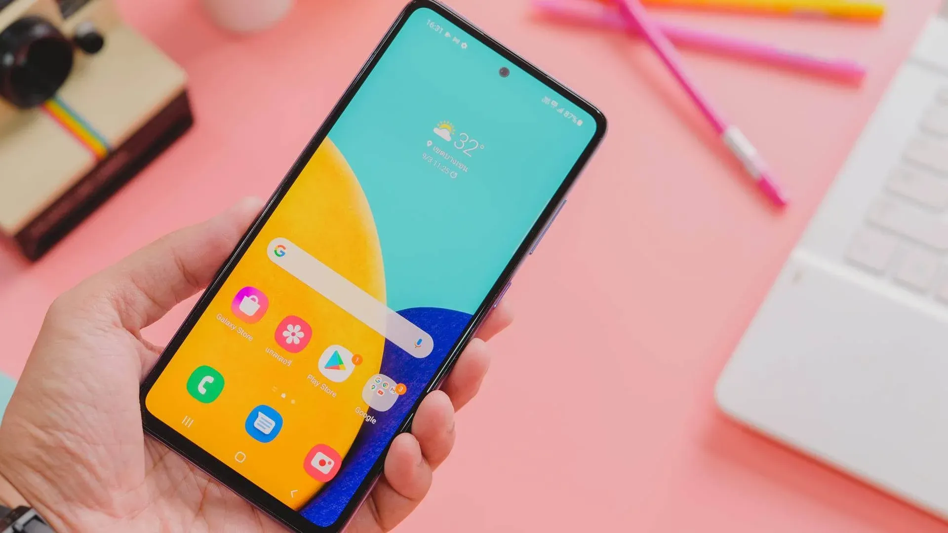 Tela do Samsung Galaxy A52 em fundo rosa ao lado de notebook