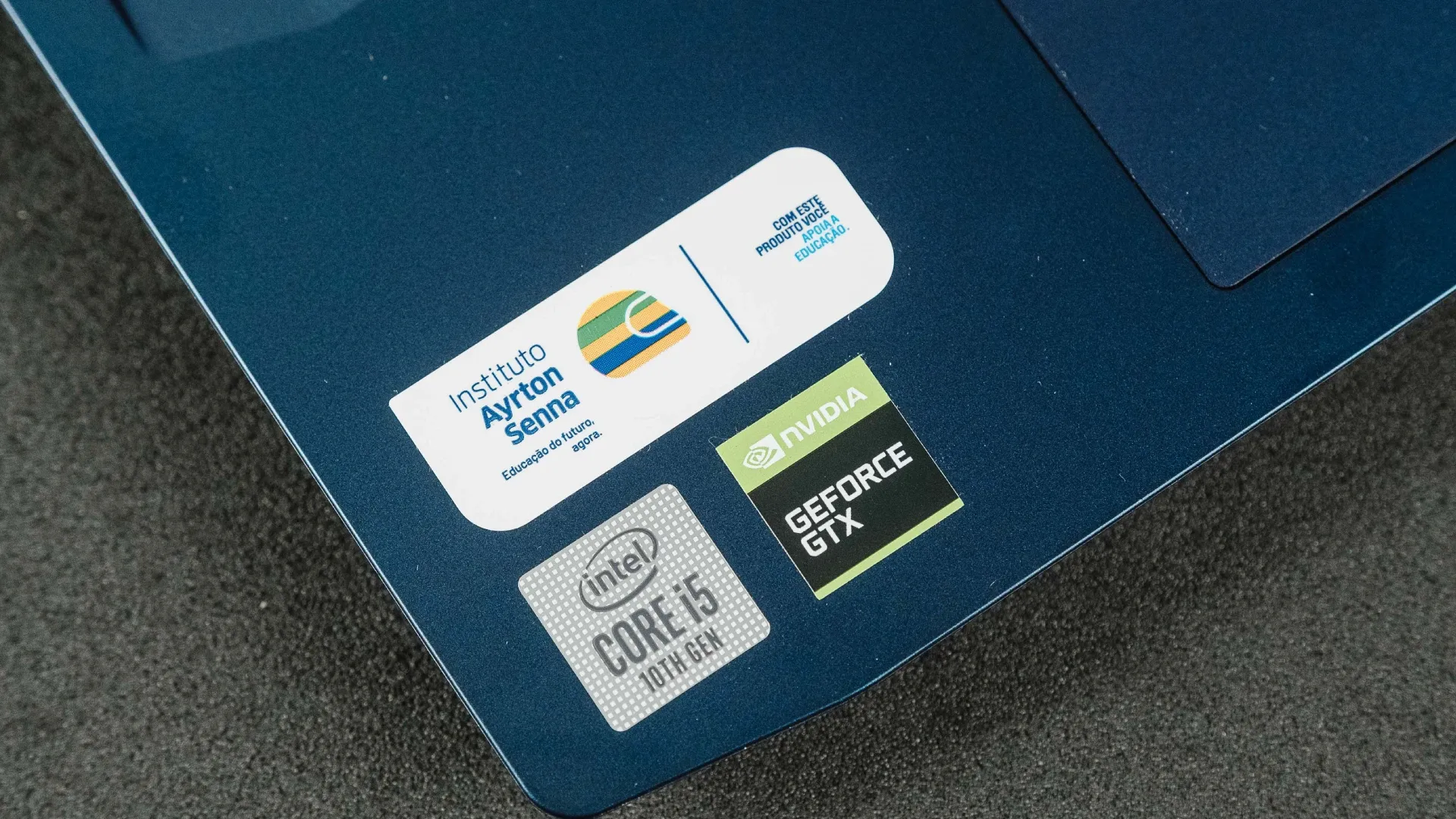 Imagem de três etiquetas do lado esquerdo do Lenovo IdeaPad Gaming 3i: Instituto Ayrton Senna, processador Intel i5 e placa de vídeo GeForce GTX