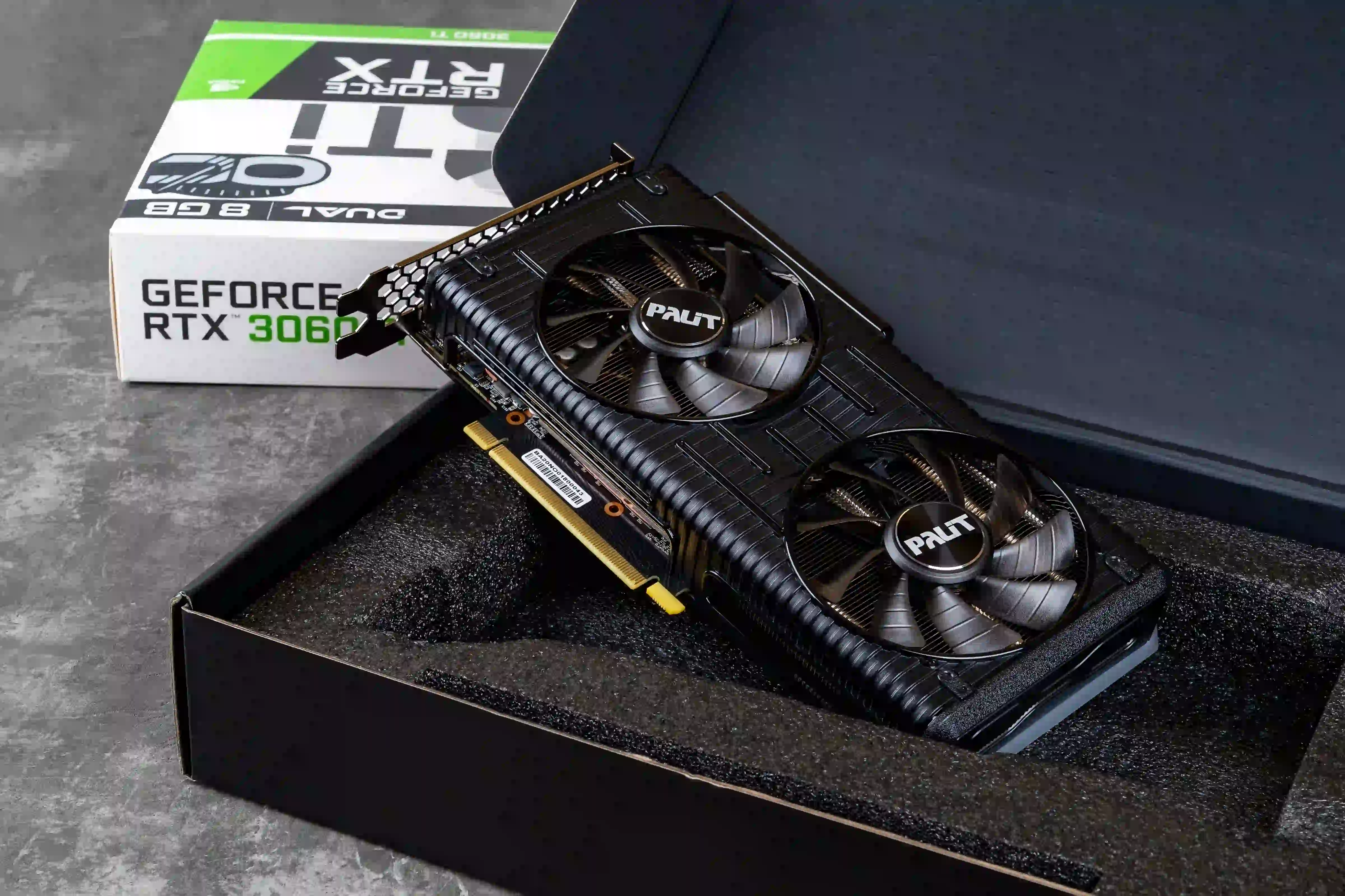 A imagem mostra uma RTX 3060 Ti, sendo retirada da caixa, com sua embalagem ao fundo.