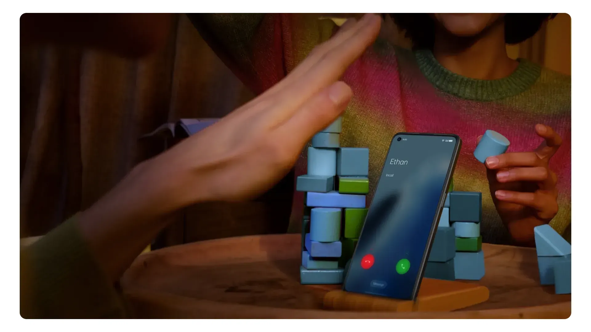 Mão de mulher fazendo gesto para atender chamada no Reno 7 sobre mesa apoiado em peças de jogo