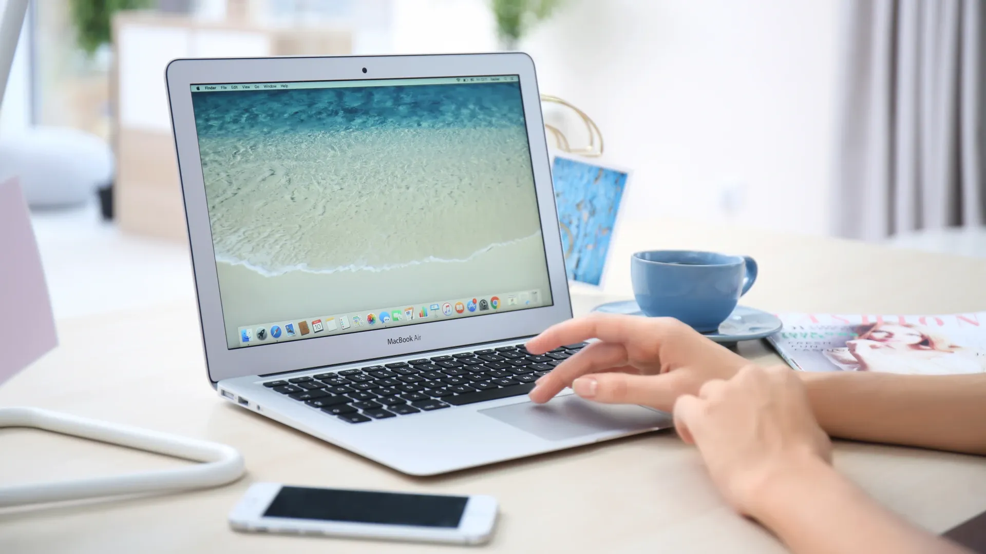 Um MacBook Air 2017 aberto sobre uma mesa junto com outros objetos enquanto uma pessoa mexe nele