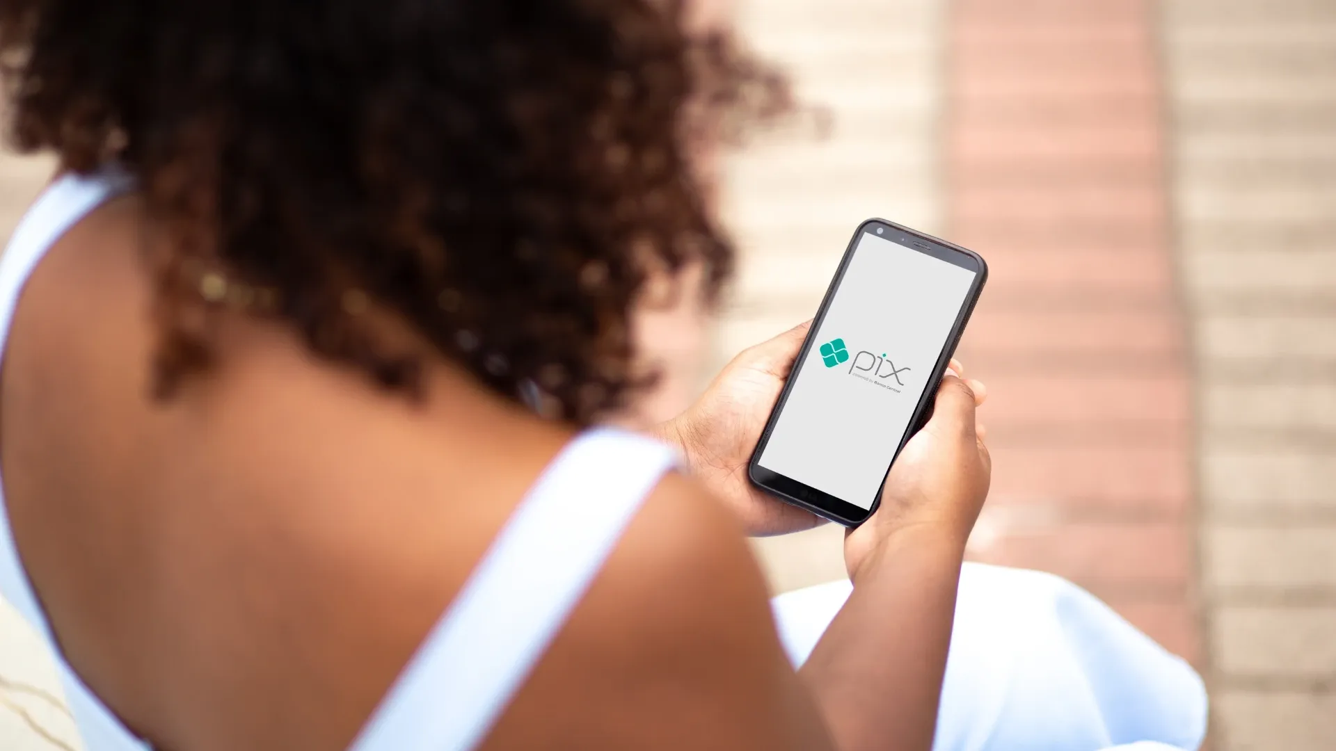 Mulher de costas com celular mostrando a logo do PIX