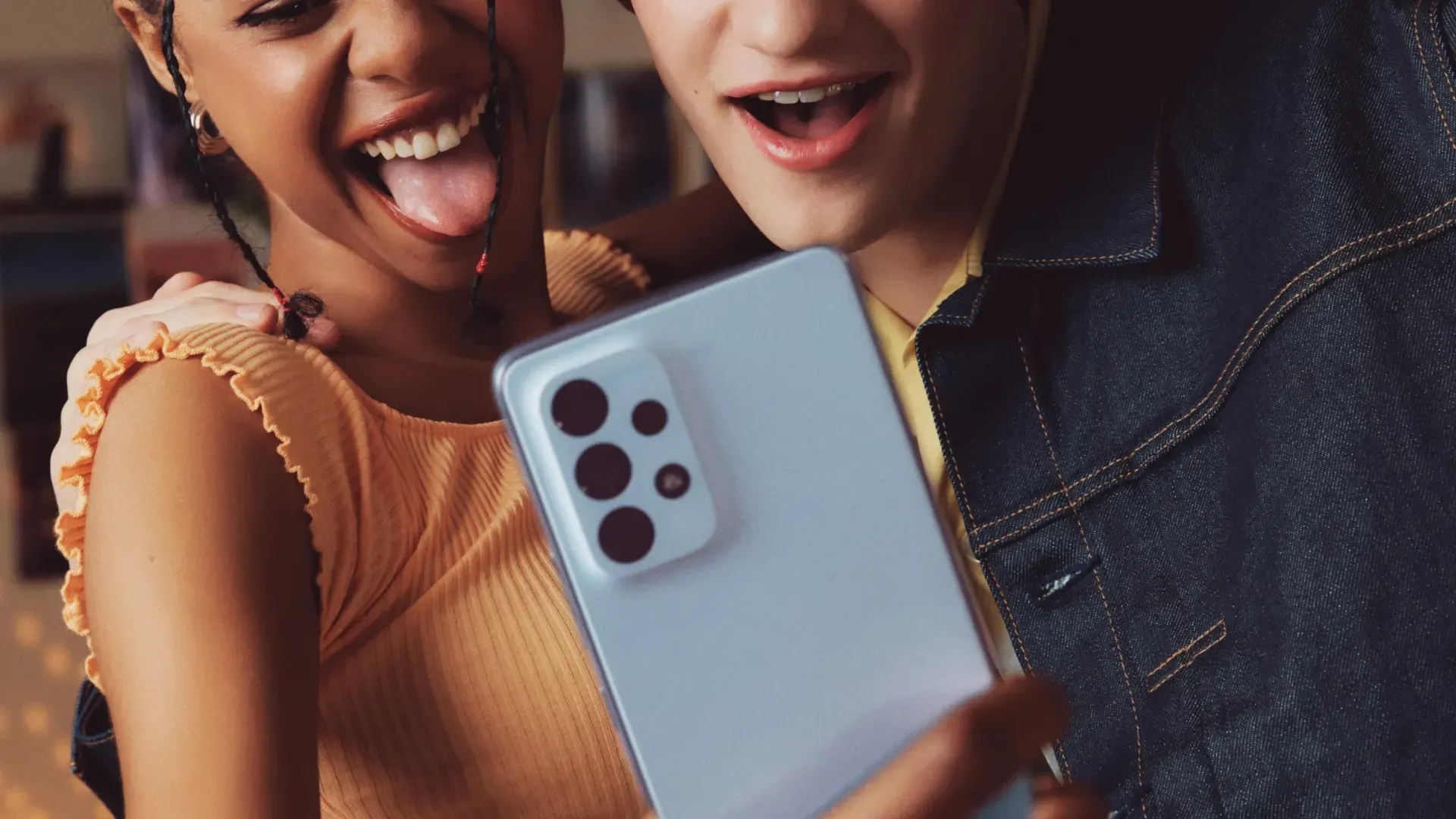 Duas pessoas sorriem enquanto olham para um celular, que está sendo segurado na vertical