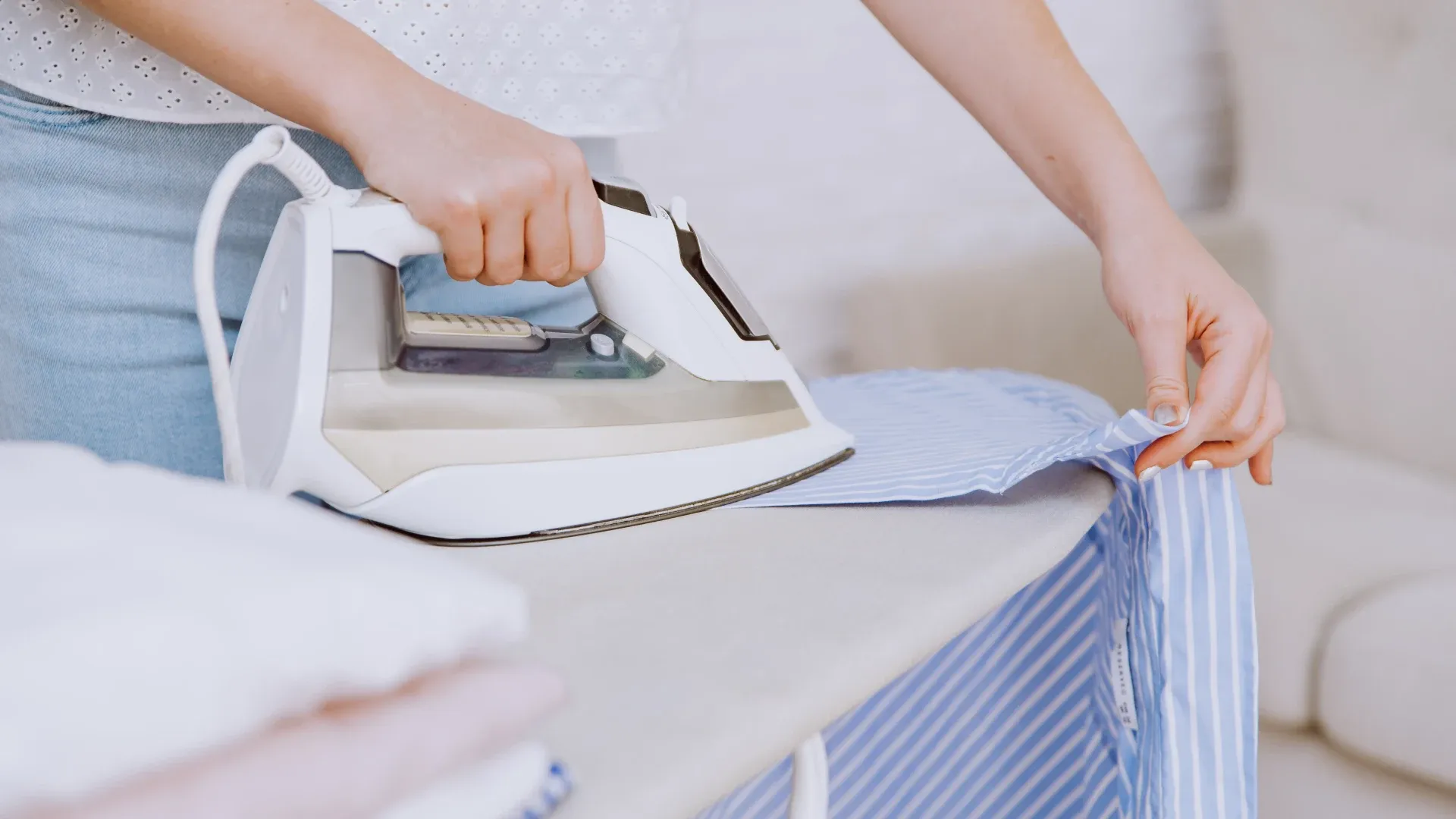 Uma mulher usa um ferro de passar roupa branco sobre uma camisa azul clara listrada
