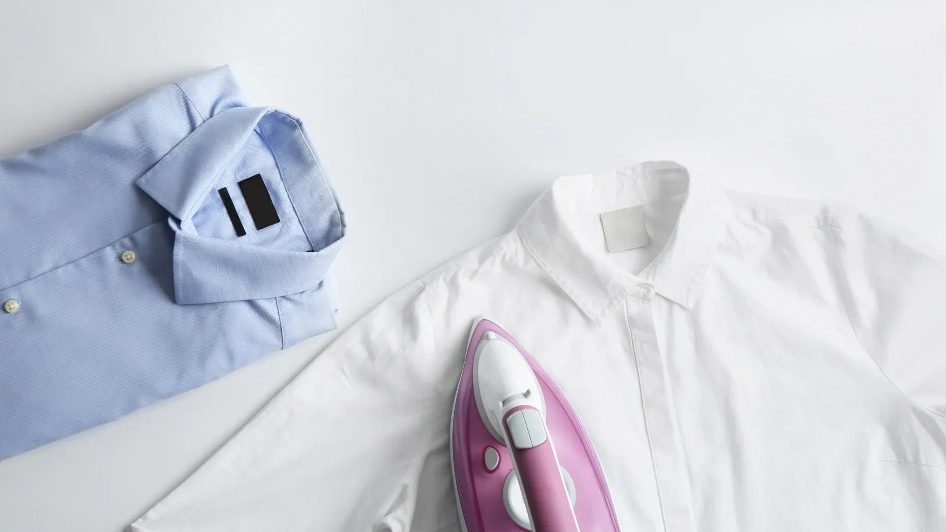 Imagem de ferro de passar roupa rosa em cima de blusa social branca