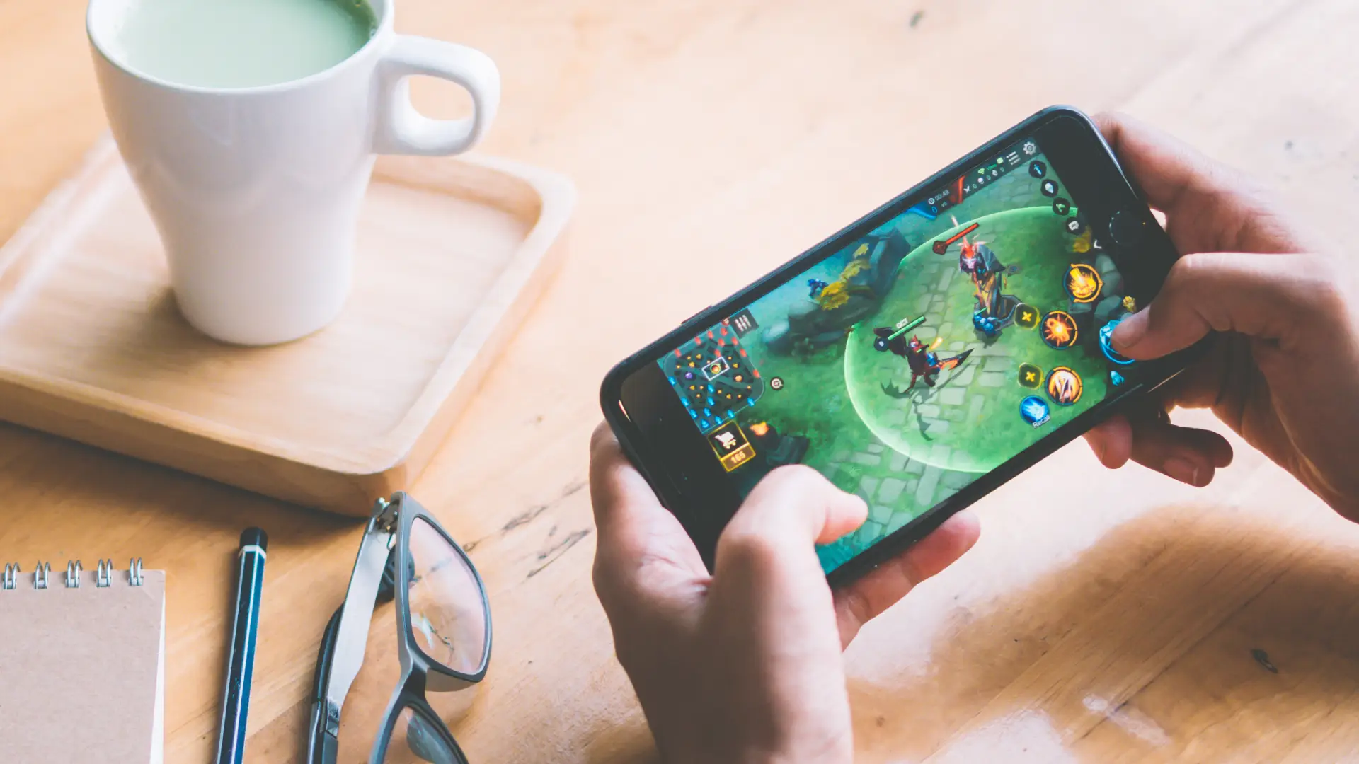 Usuário jogando game em seu iPhone 8 usado sobre mesa ao lado de xícara