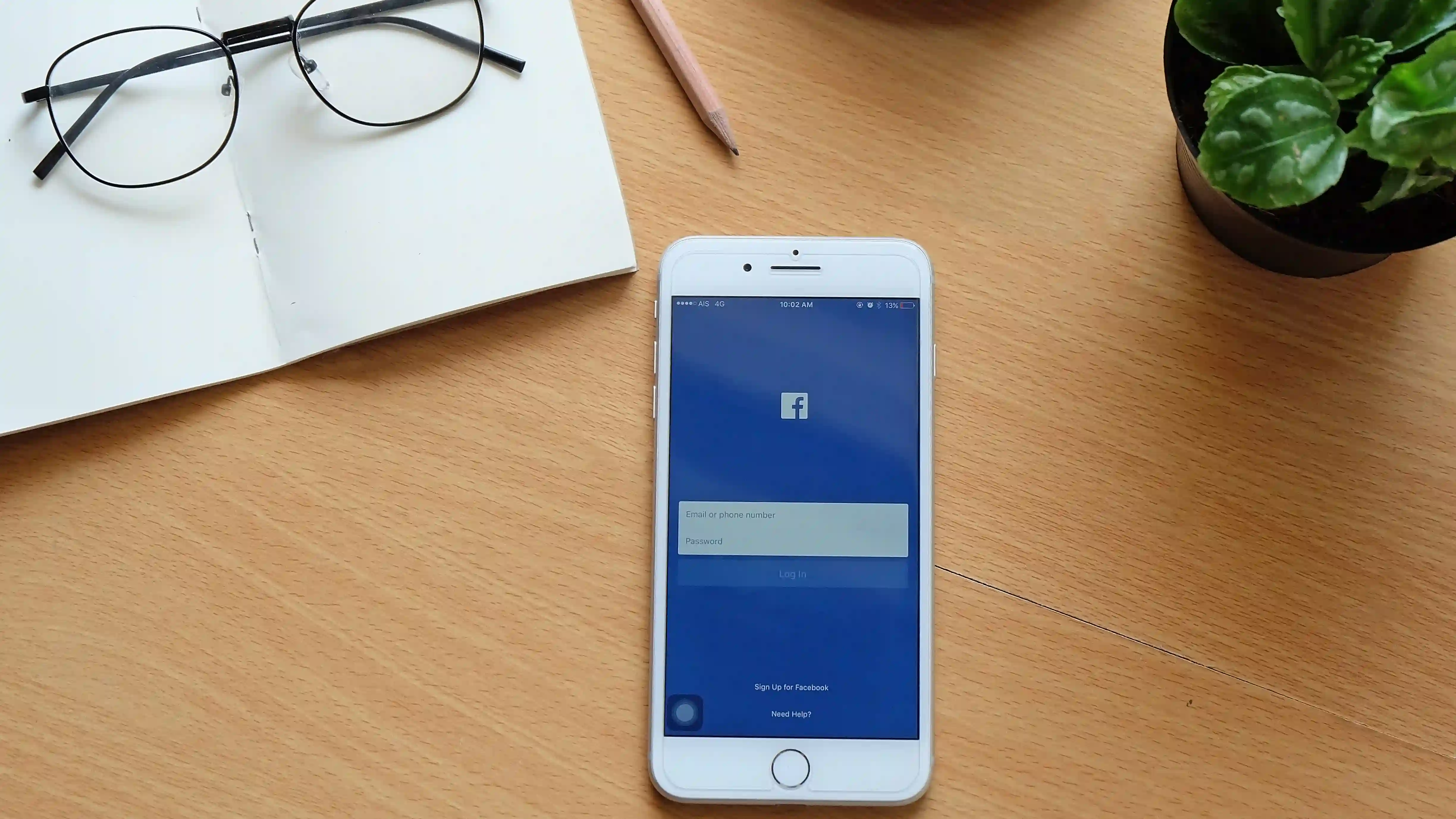 iPhone 7 Plus usado sobre mesa ao lado de vaso de plantas e óculos