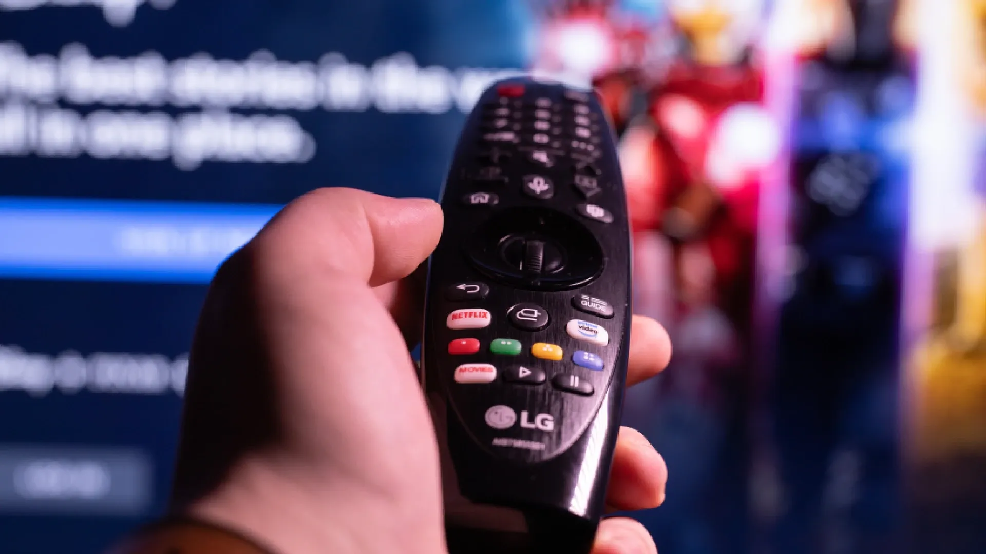 Mão masculina em primeiro plano segurando controle Smart Magic da LG apontando para tela desfocada ao fundo