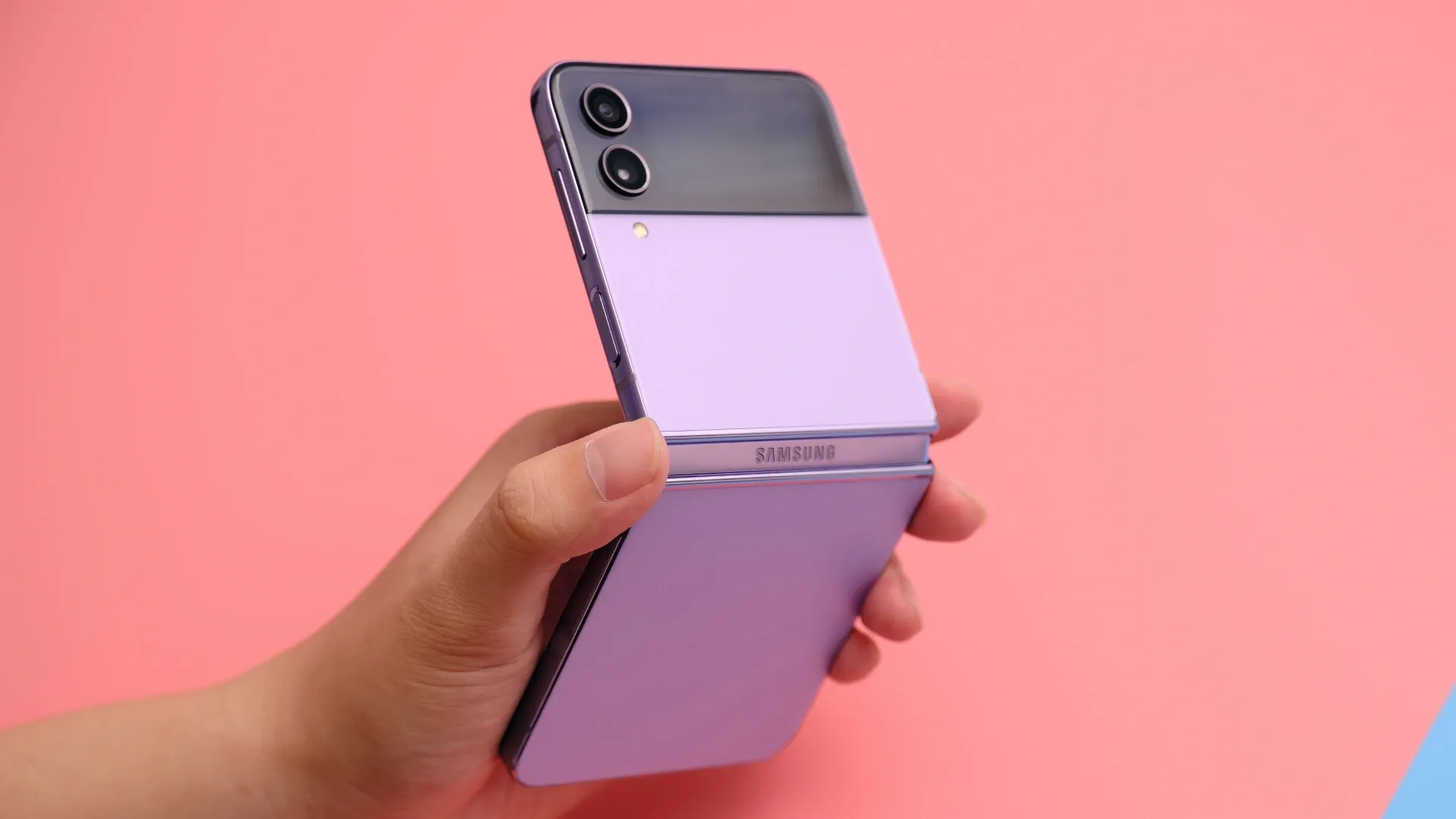 Um celular de cor roxa está sendo segurado por uma mão, em frente a um fundo de cor laranja