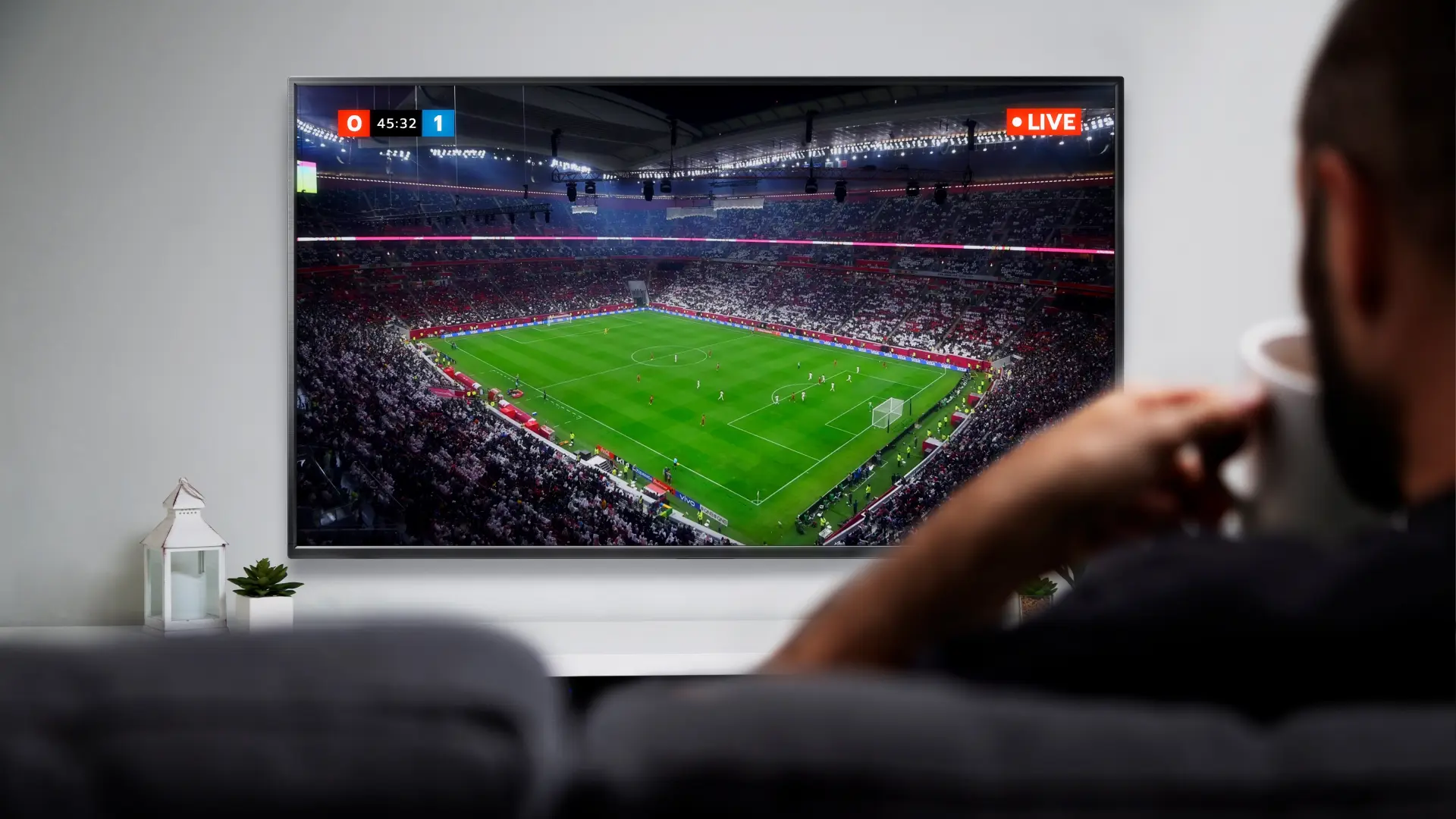 Homem branco e de cabelo curto castanho assistindo televisão enquanto está sentado em um sofá.