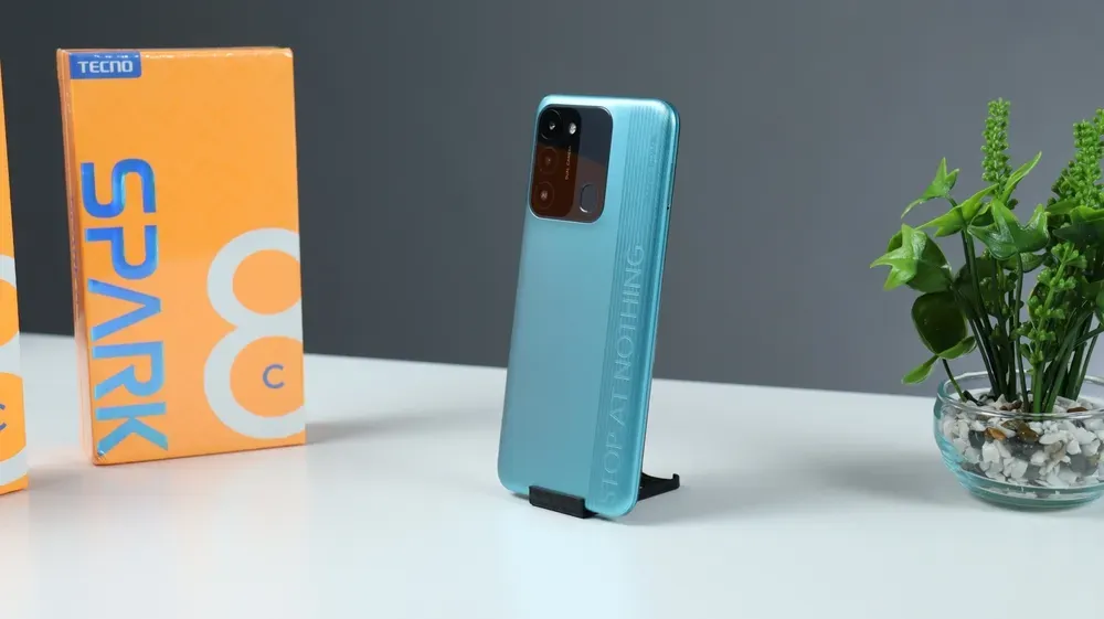  Celular Tecno Spark 8C ao lado de caixa e vaso de planta