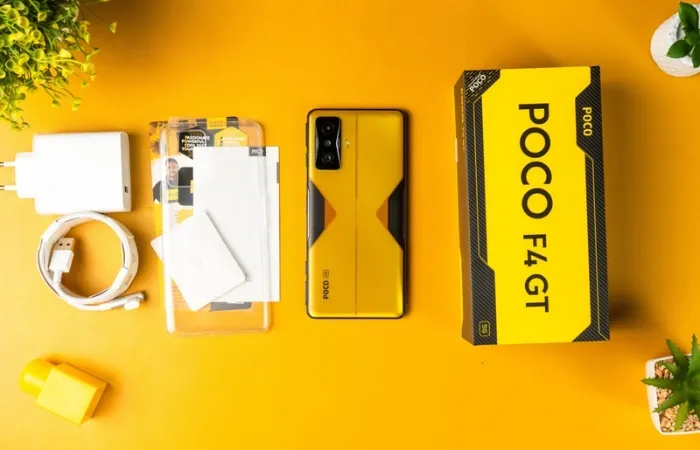 Poco F4 GT ao lado de sua caixa e demais acessórios em mesa amarela