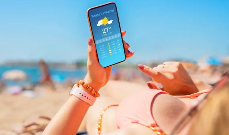 Mulher usa celular na praia, sob o sol