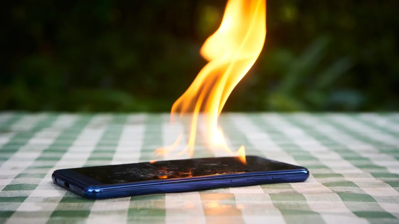 Celular pegando fogo sobre mesa com toalha quadriculada verde e branco