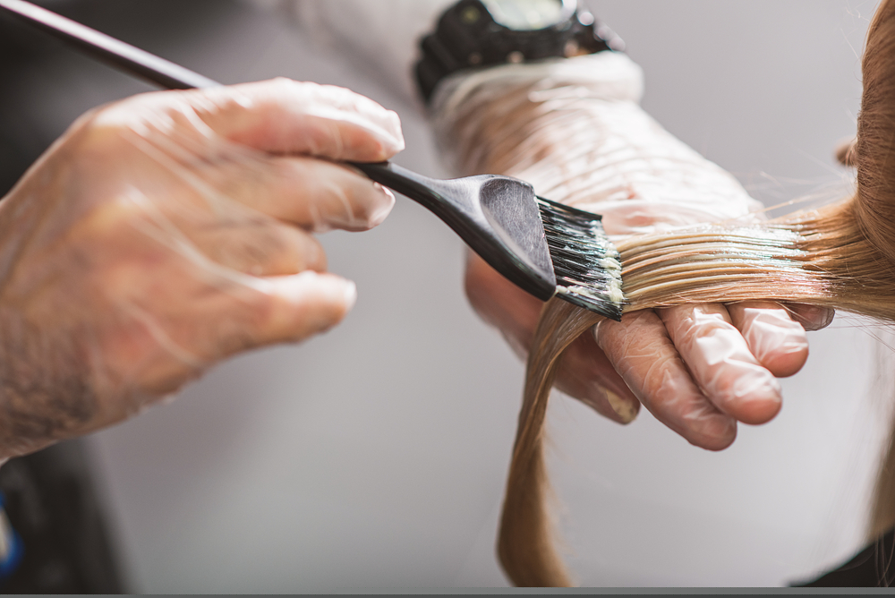 mãos masculinas pintando cabelo de mulher com pincel