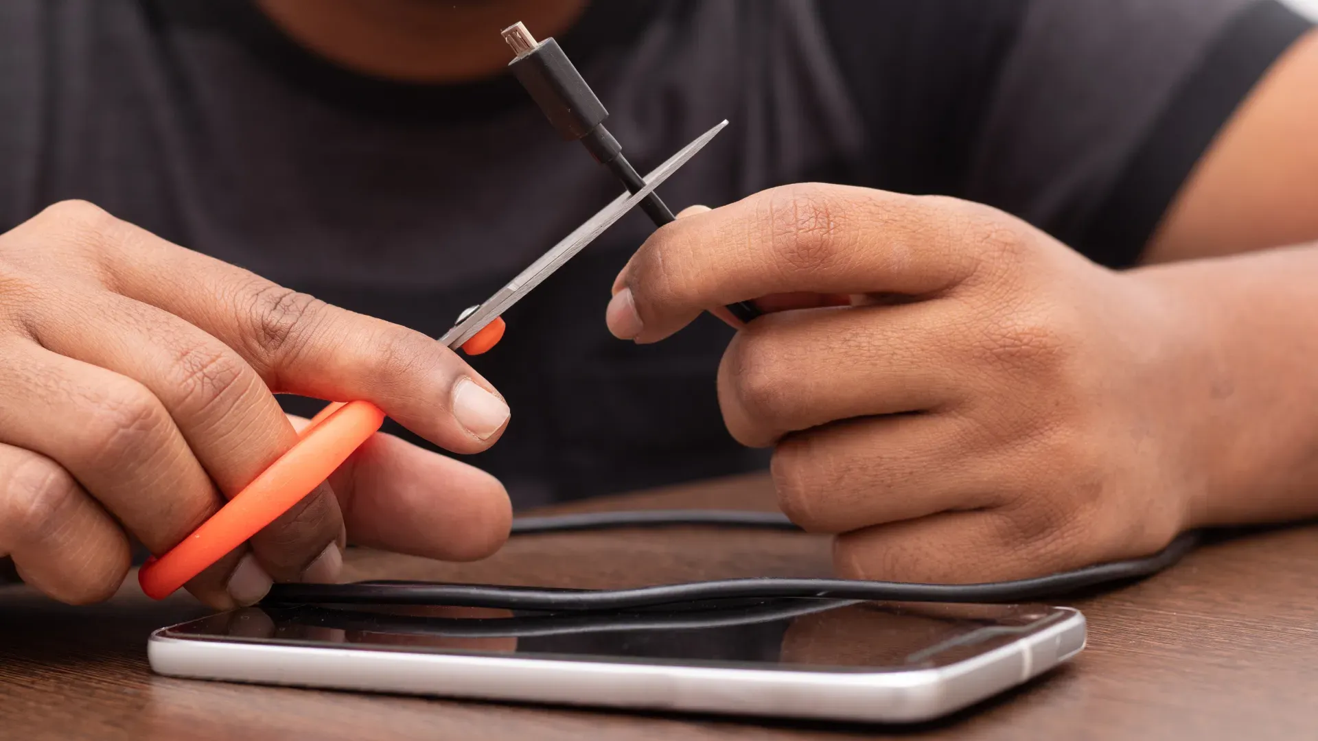 Homem cortando o carregador de um celular