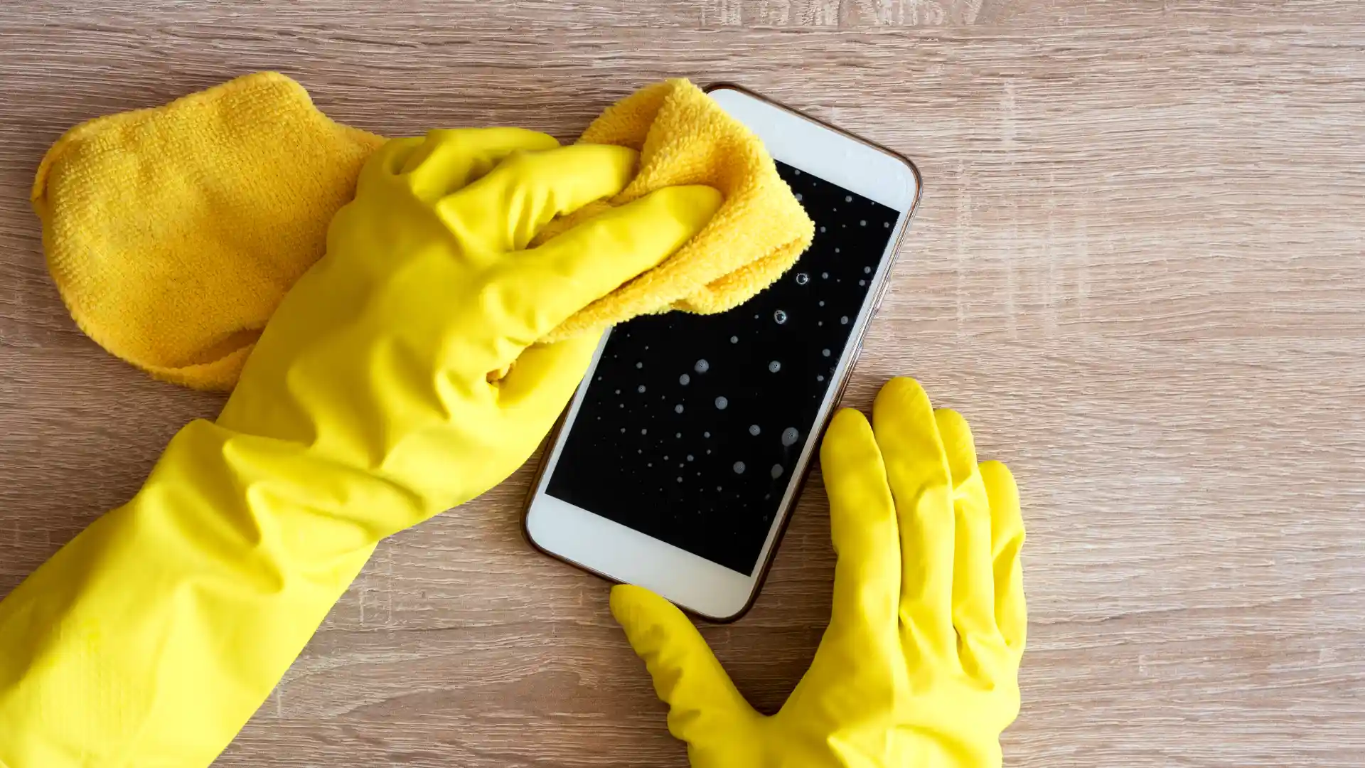 Mãos usando luvas de borracha limpando um celular