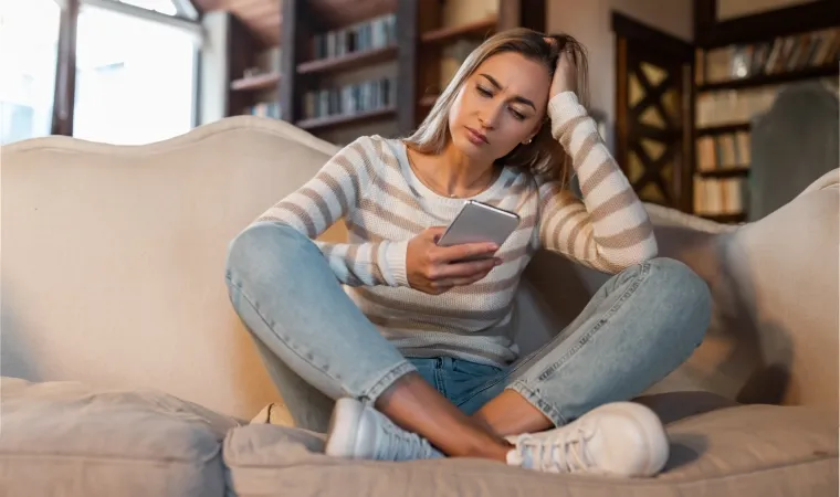 Mulher com feição de preocupada olhando para tela de um celular.