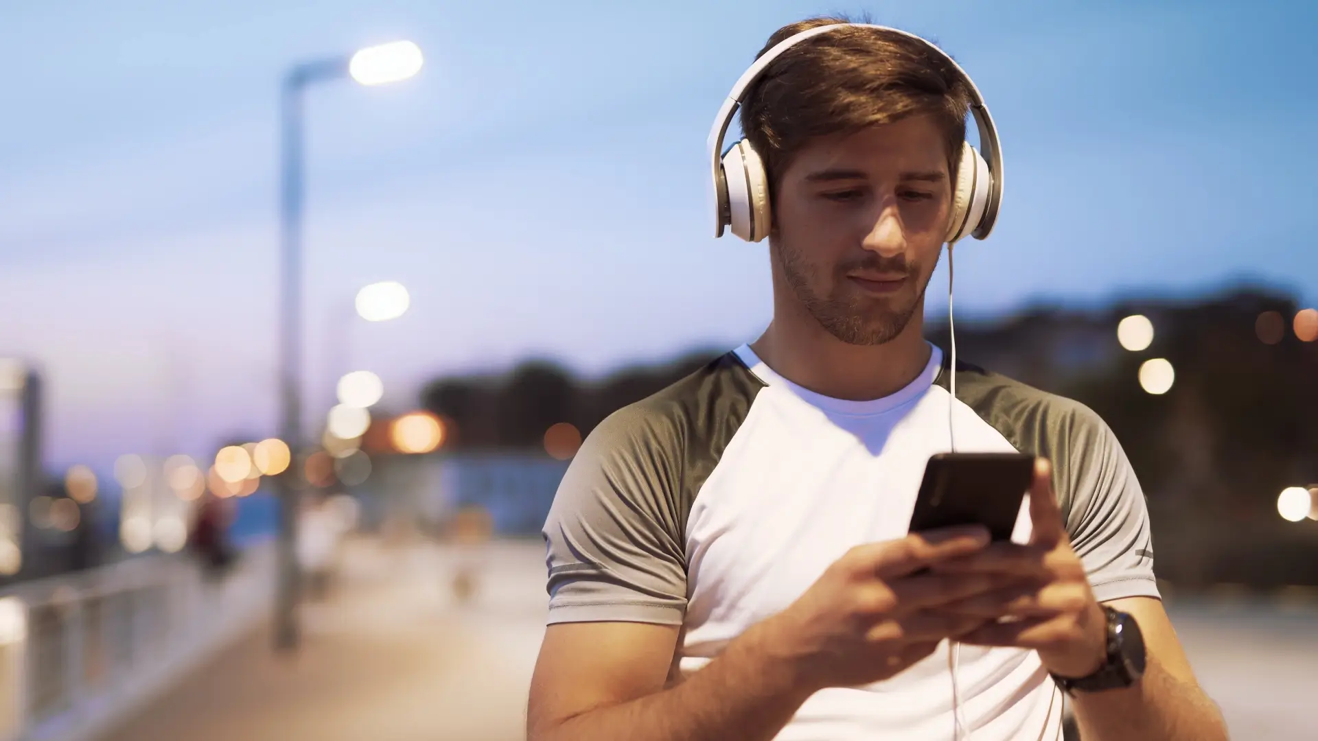 Homem branco mexendo no celular enquanto usa fones de ouvido na rua
