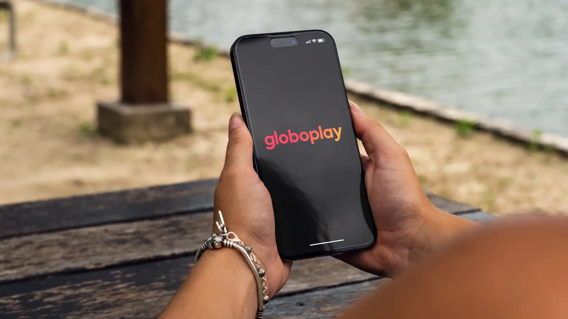 Mão feminina segurando um telefone mostrando 'Globoplay' escrito na tela