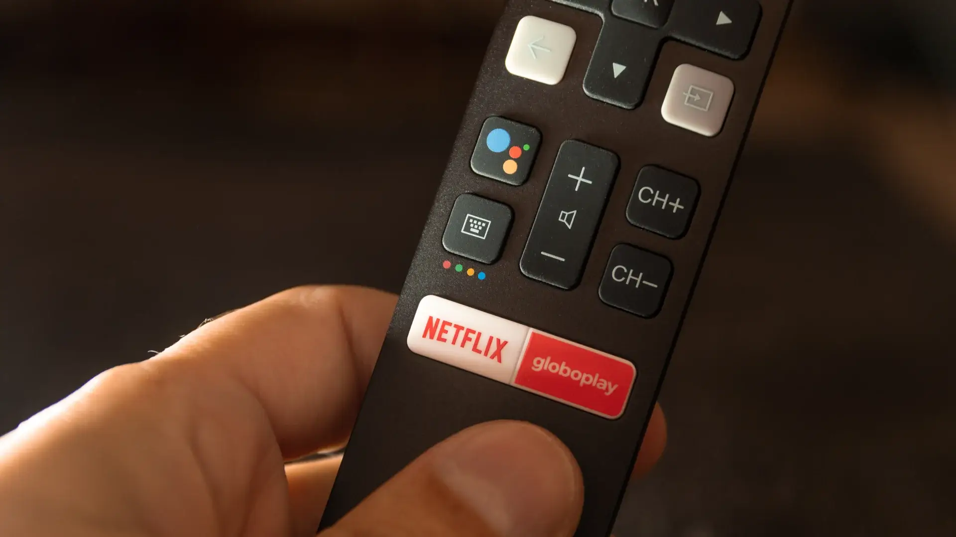 Close em mão segurando controle remoto de TV com botão dedicado ao Globoplay