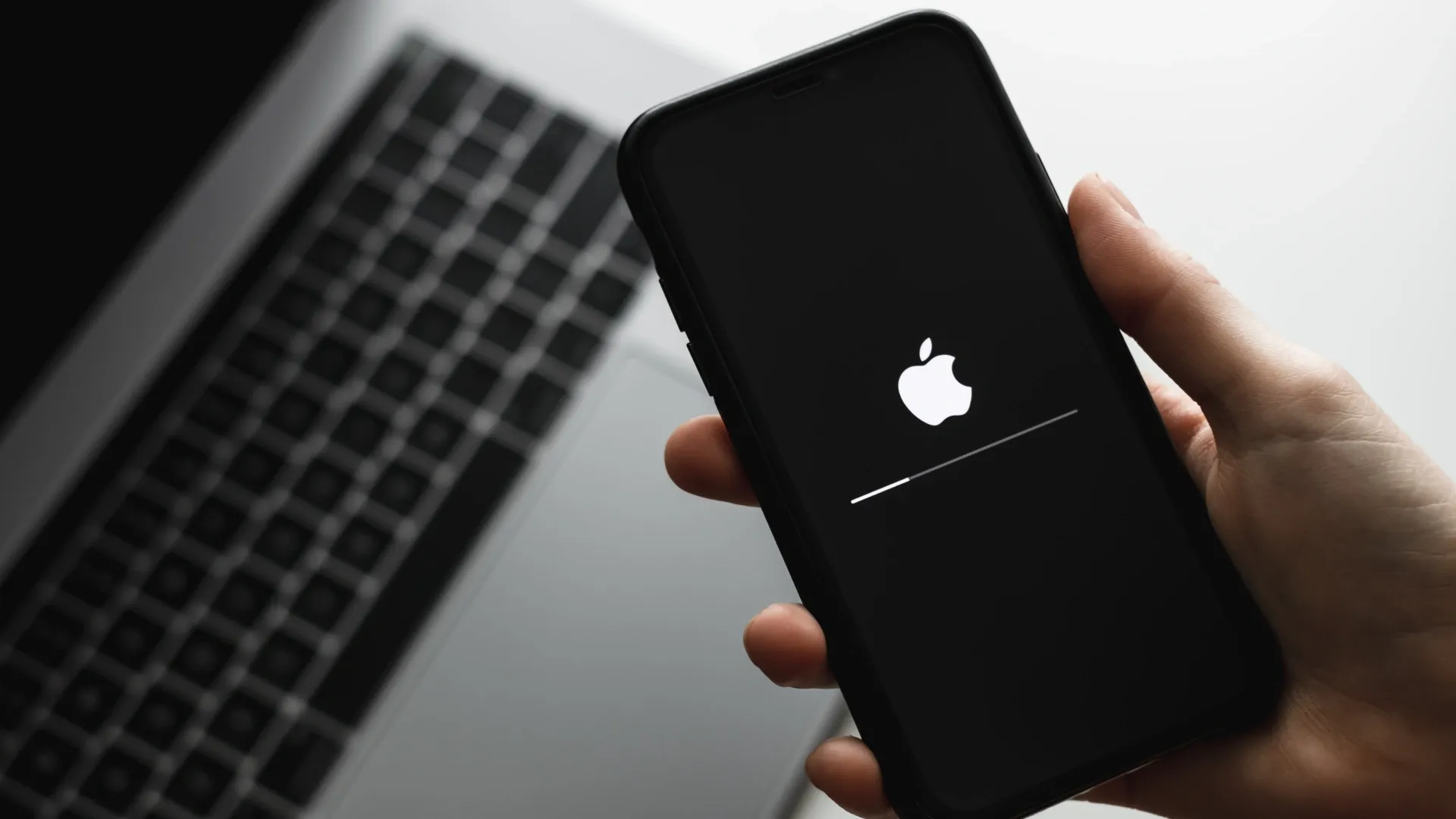 Uma pessoa segura um iPhone, que está reiniciando a tela. No aparelho aparece a imagem de uma maçã mordida