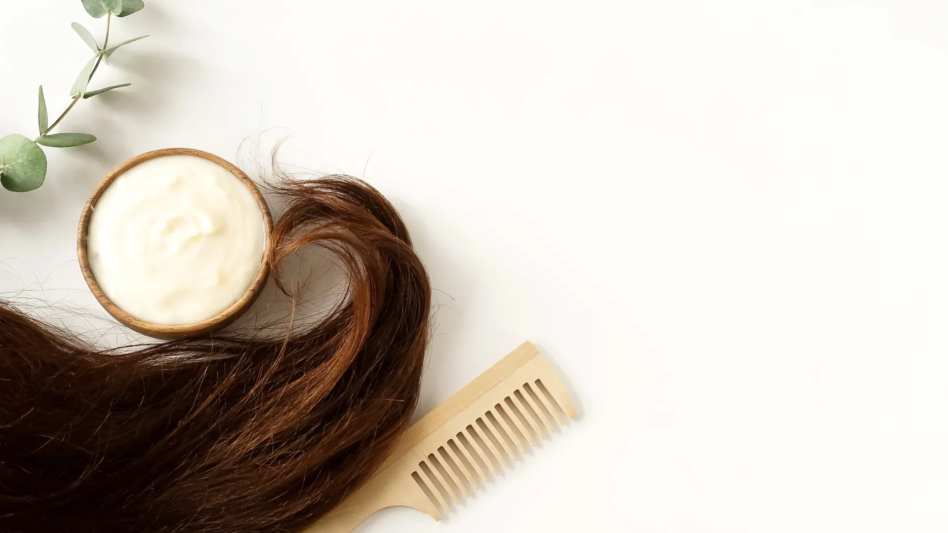 Pote de creme de cabelo, ao lado de um pente, uma folha e cabelos femininos