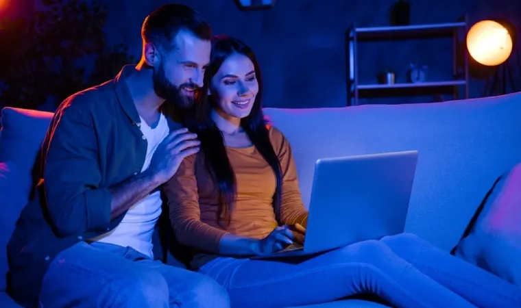 Casal sentado em sofá assistindo algo em um notebook