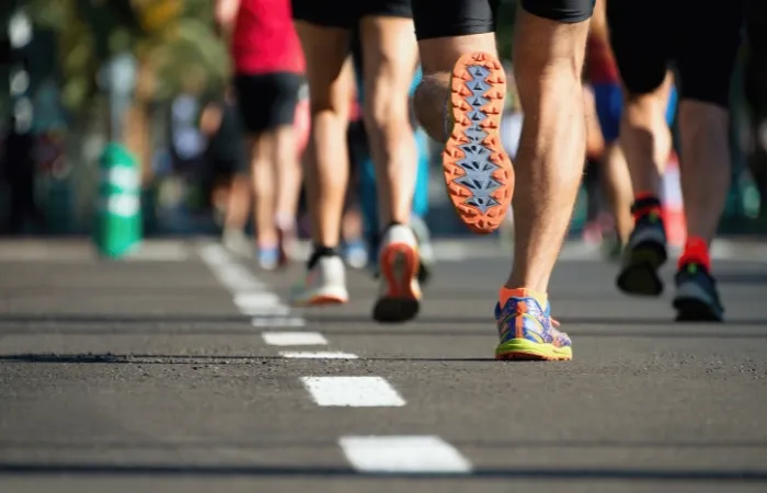 Uma visão aproximada das pernas e pés de vários corredores usando tênis esportivos, capturada em movimento durante uma corrida de rua.