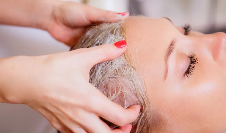Close em mãos passando máscara reconstrutora no cabelo de uma outra pessoa.