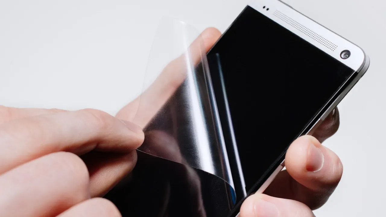 Pessoa com celular na mão tirando película da tela