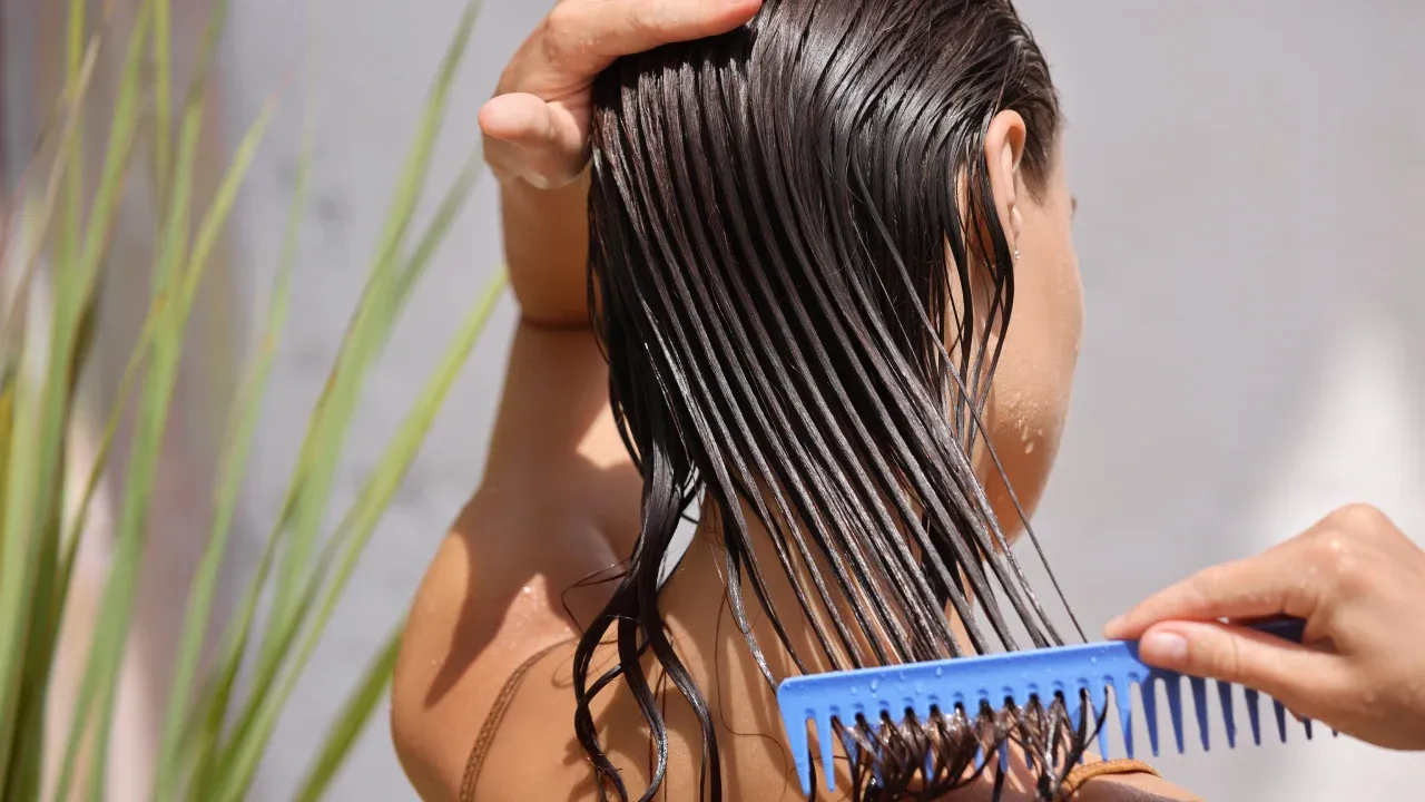 Mulher branca penteando o cabelo liso e molhado com um pente azul