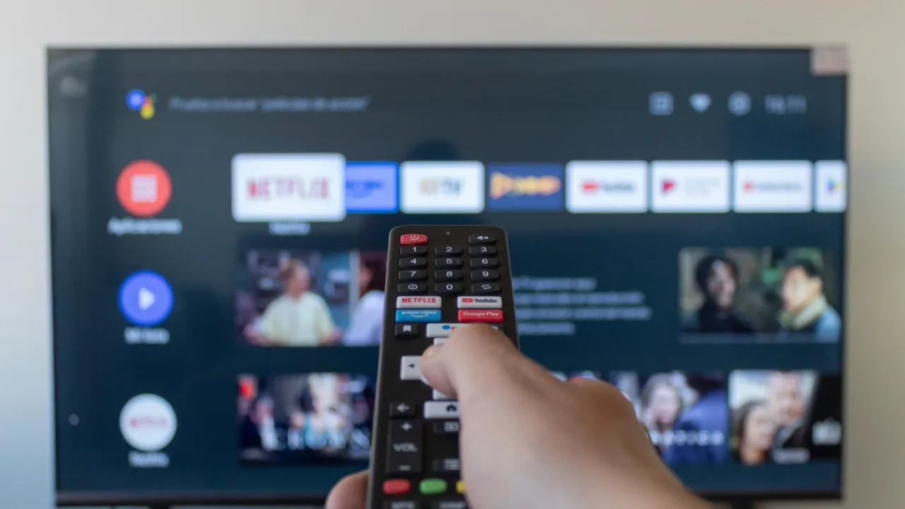 Imagem de uma pessoa segurando um controle de TV na frente de vários apps de streaming