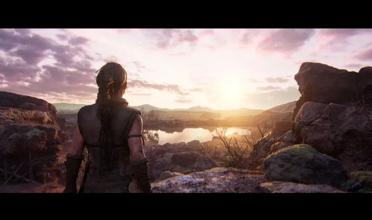 Imagem de Hellblade 2 com a protagonista Senua de costas apreciando o nascer do Sol em uma bela paisagem com reflexos na água e pedras ao redor