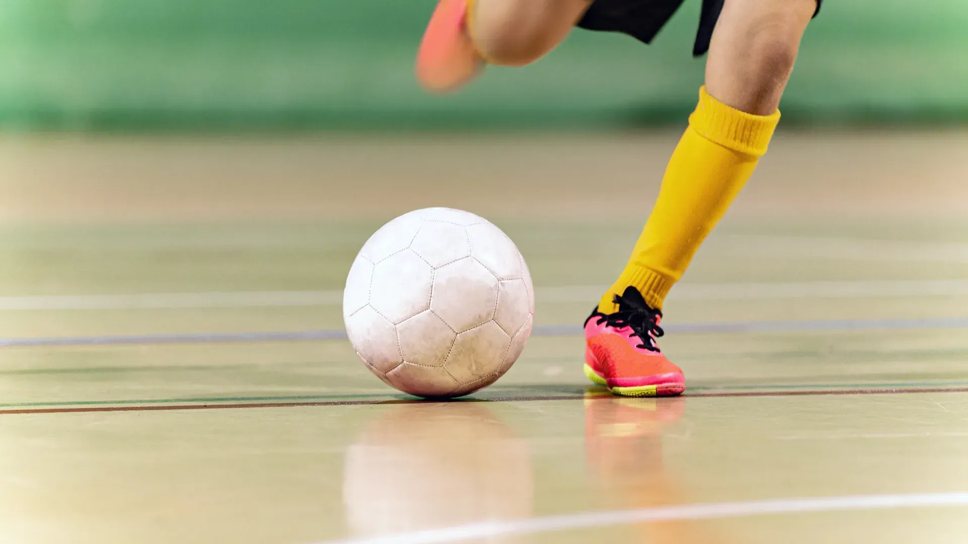 Close em pernas masculinas chutando uma bola de futsal em campo de futsal à luz do dia
