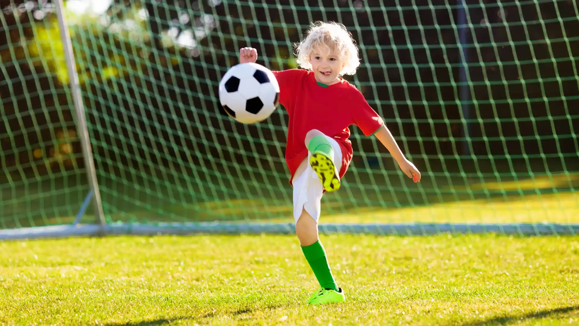 Criança jogando futebol em campo ao ar livre com gol ao fundo