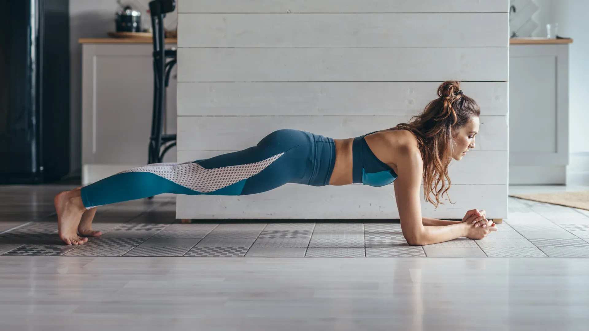 Mulher na cozinha de casa executando prancha ventral