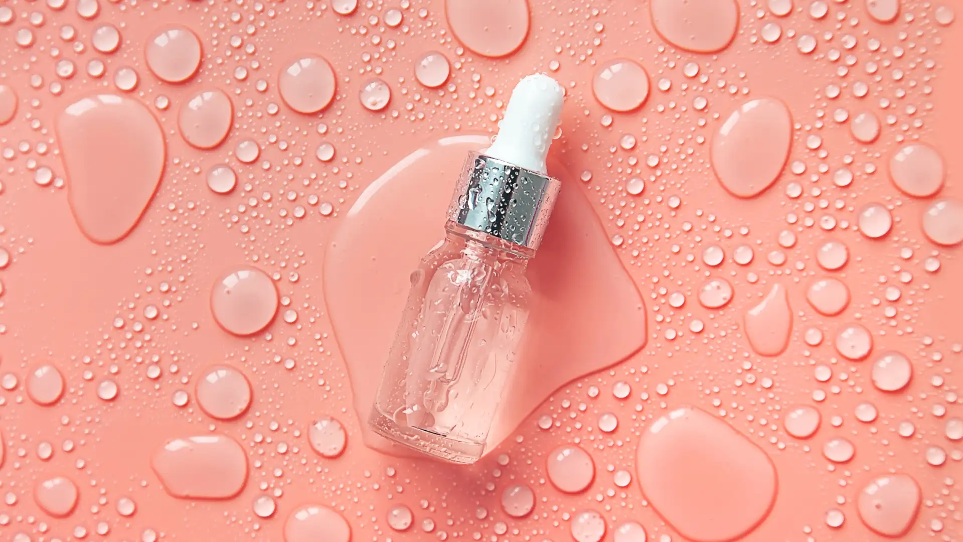 Frasco de um produto líquido de cosmético com gotas espalhadas ao redor em um fundo laranja