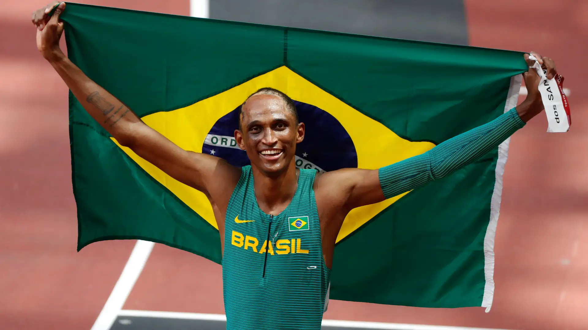 Imagem de um homem negro com roupas atléticas segurando a bandeira do Brasil nas costas