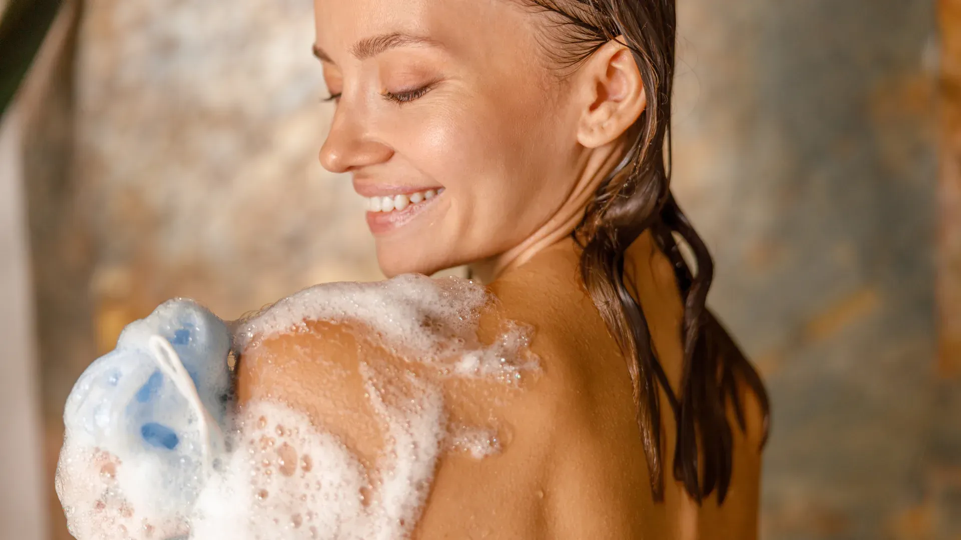 Close em mulher loira esfregando bucha com sabão no ombro durante banho