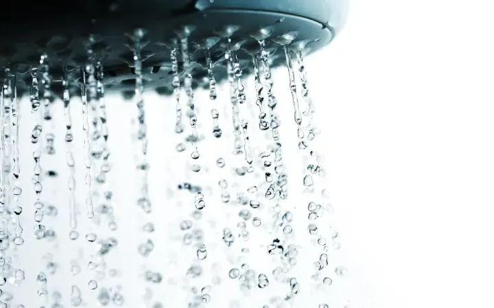 Um chuveiro visto de perto com água caindo sobre um fundo branco.