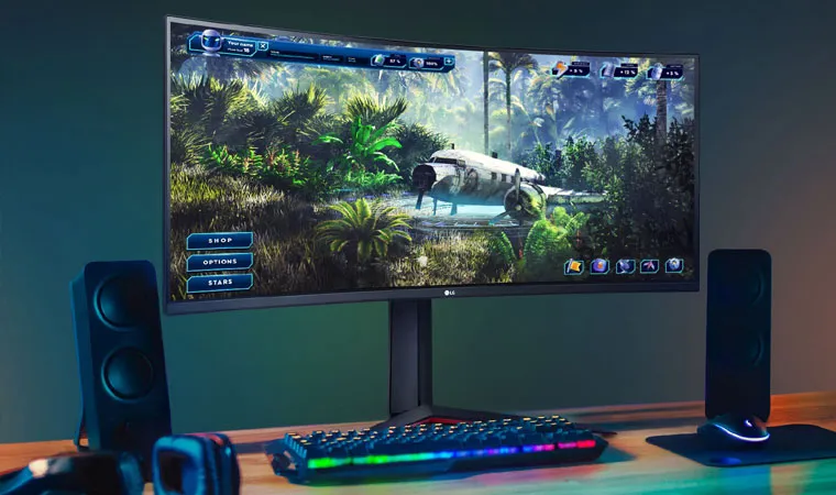 Foto do monitor gamer LG WQHD UltraGear 34GP63A-B sobre uma mesa com teclado gamer e caixas de som.