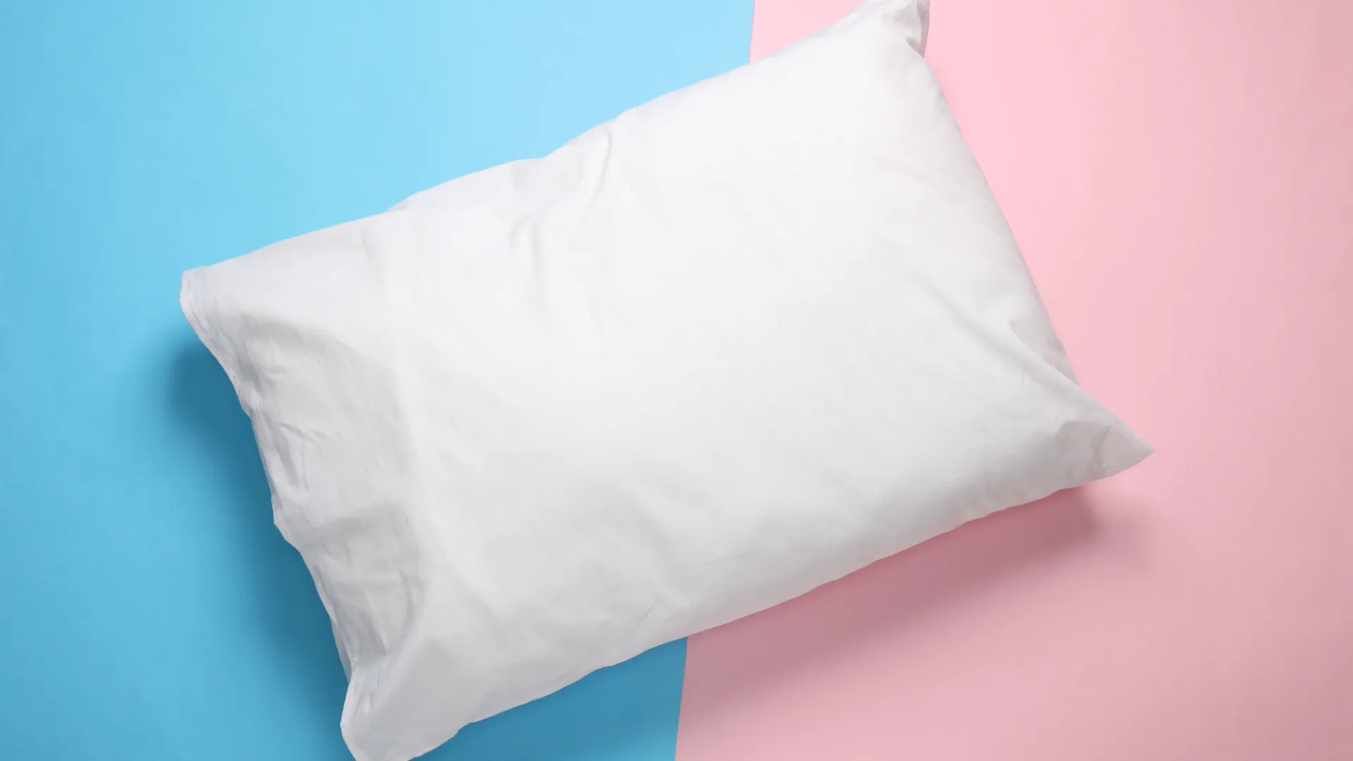Travesseiro branco apoiado em fundo dividido pelas cores rosa e azul