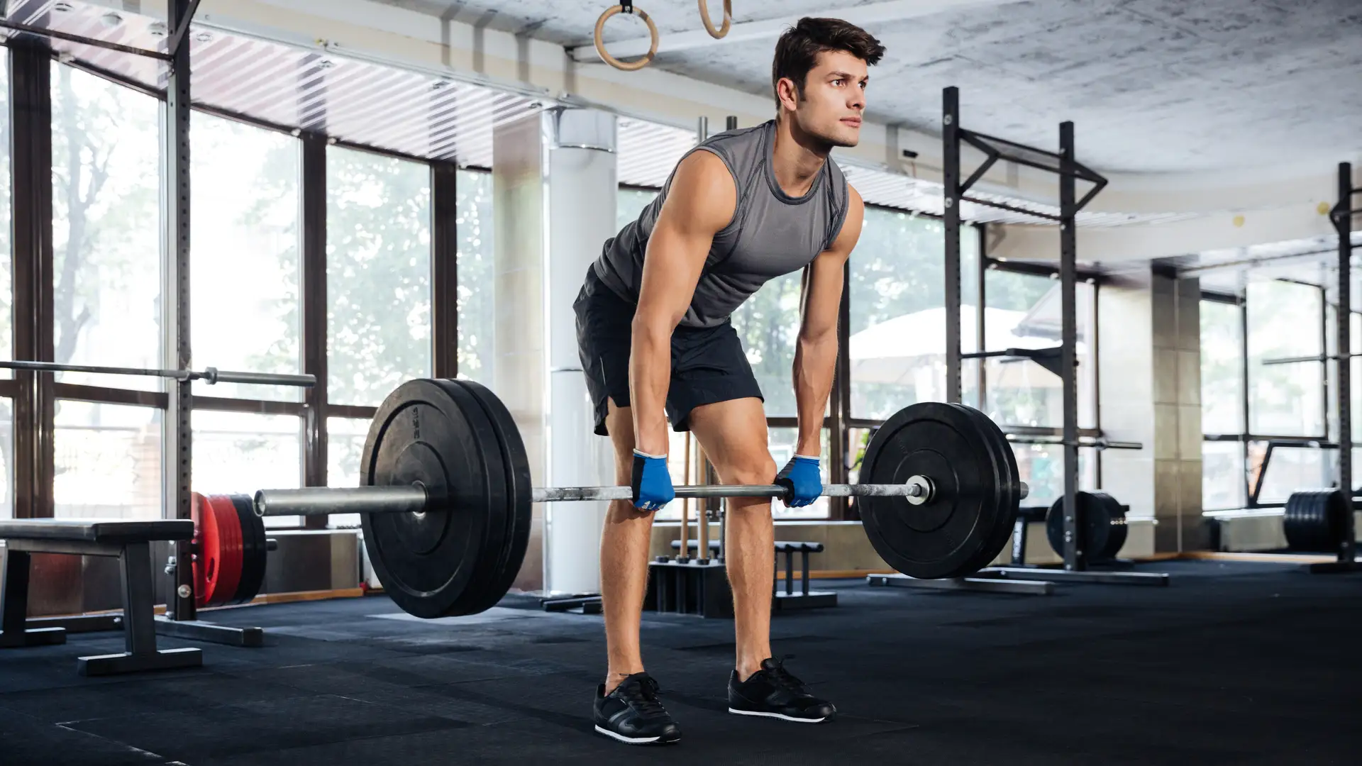 Homem em academia fazendo treino de perna com barra e anilhas