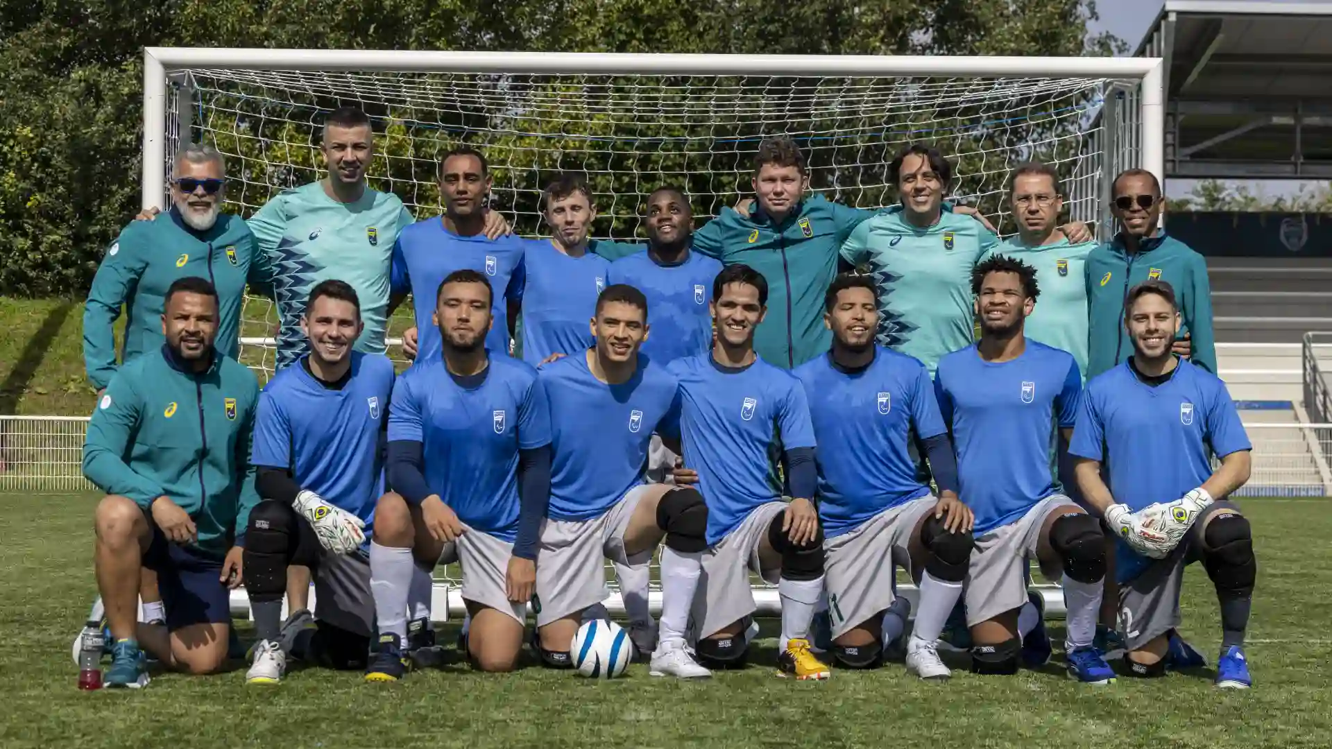 Grupo de homens jogadores de futebol em frente a um gol no campo de futebol à luz do dia