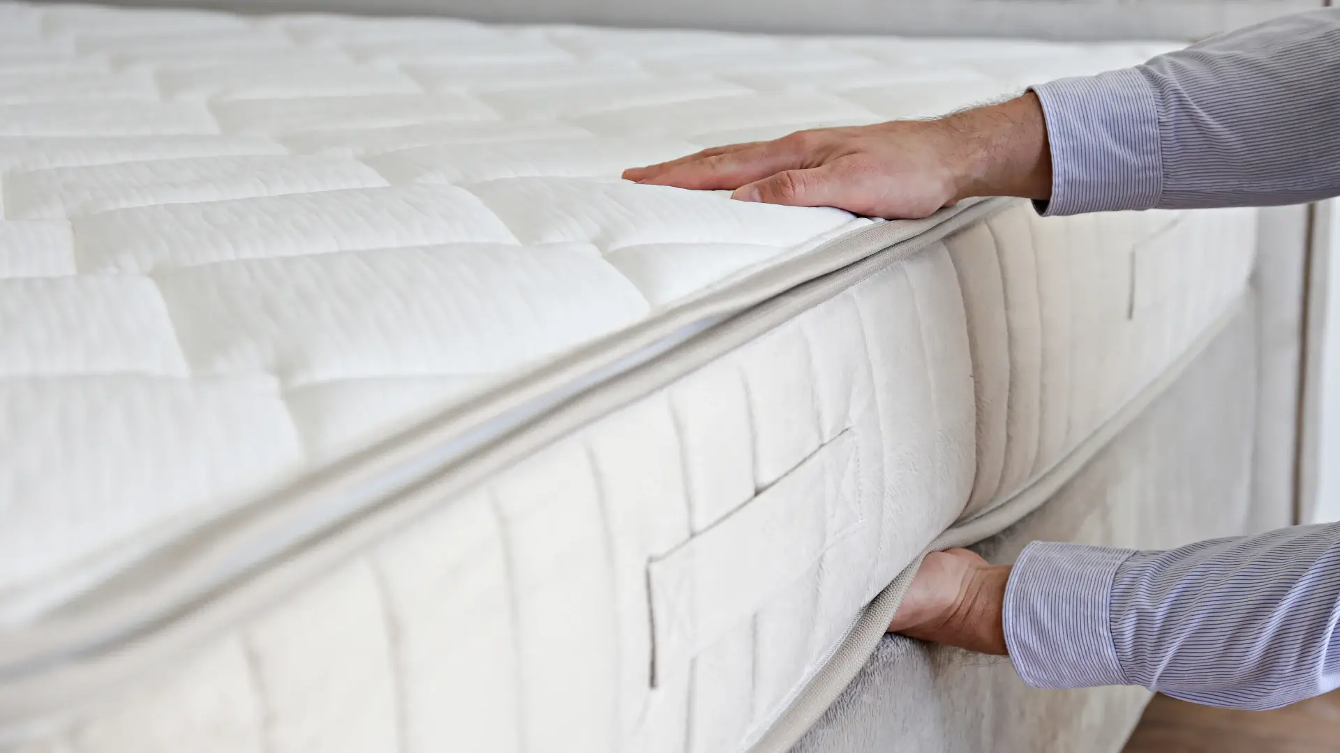 Pessoa mexendo em colchão branco com as duas mãos