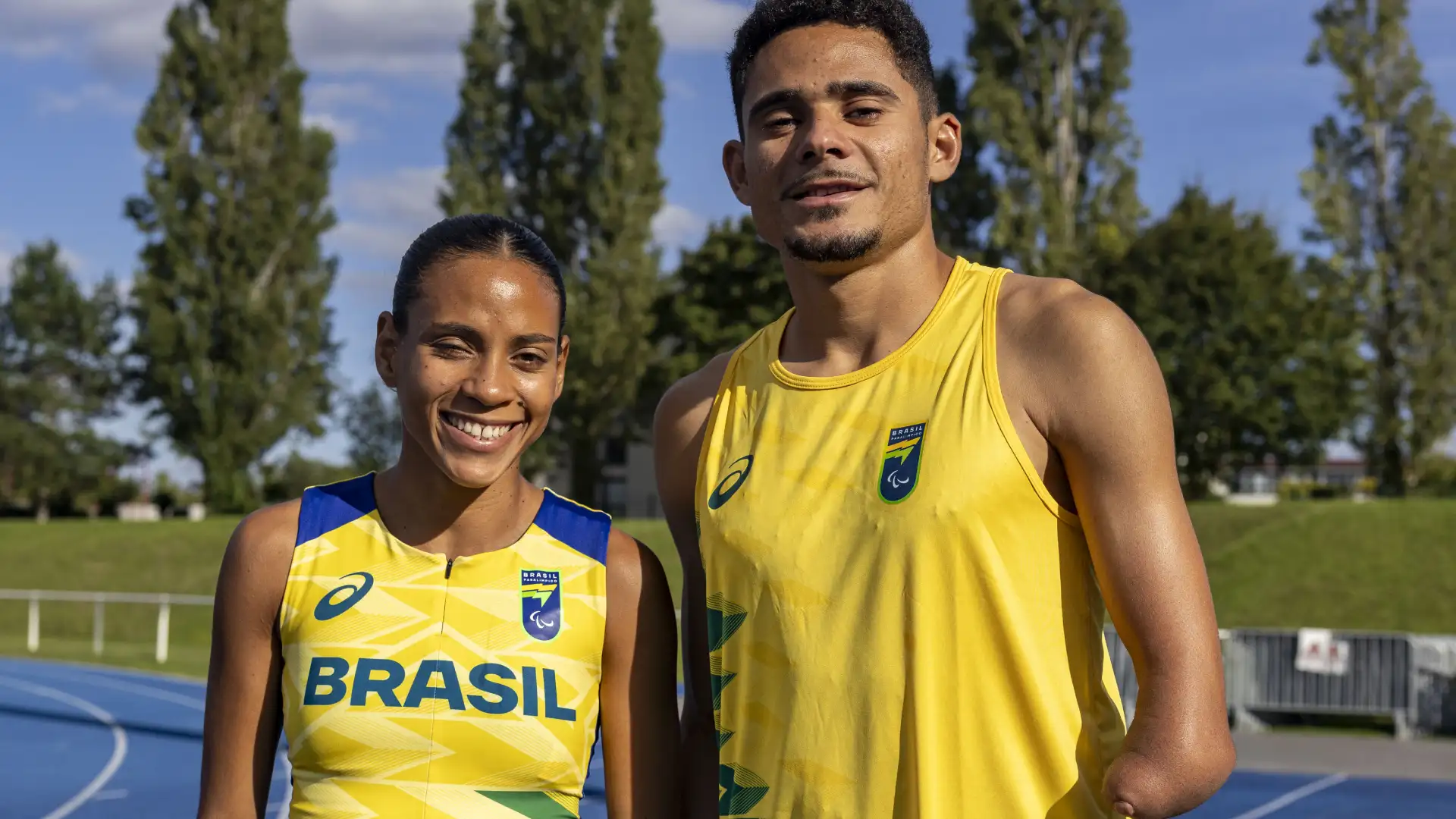 Homem e mulher sorriem ao ar livre em uma pista de atletismo à luz do dia