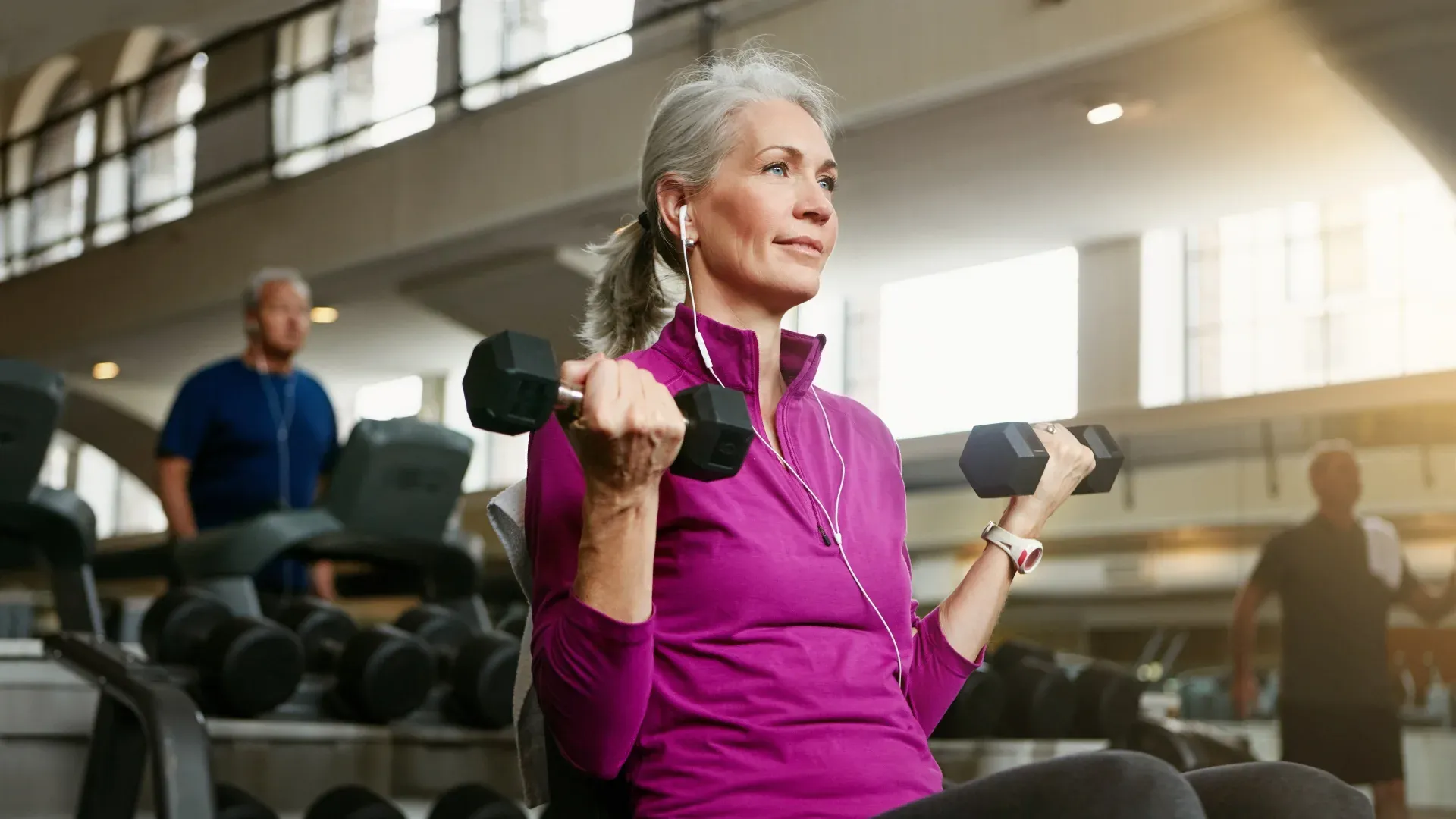 Mulher de cabelos brancos fazendo exercício de bíceps com halteres na academia