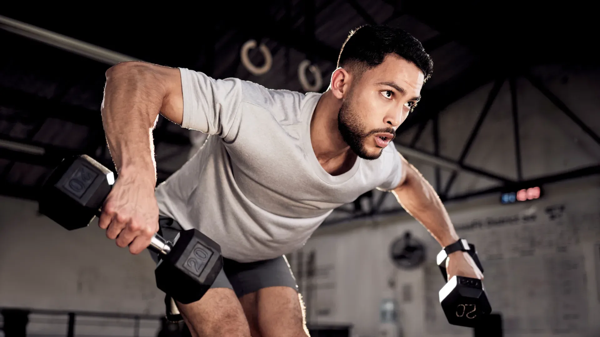 Homem fazendo treino de ombro com halteres de 20kg em cada mão dentro da academia